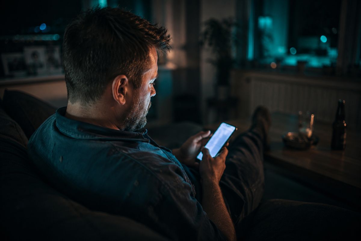 Handwerker sitzt abends auf dem Sofa und scrollt am Smartphone